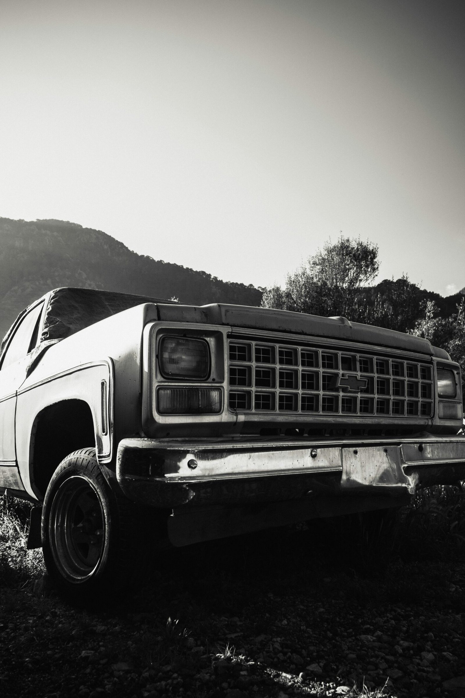 Black and white photo of an abandoned vintage pickup truck in a mountainous landscape.