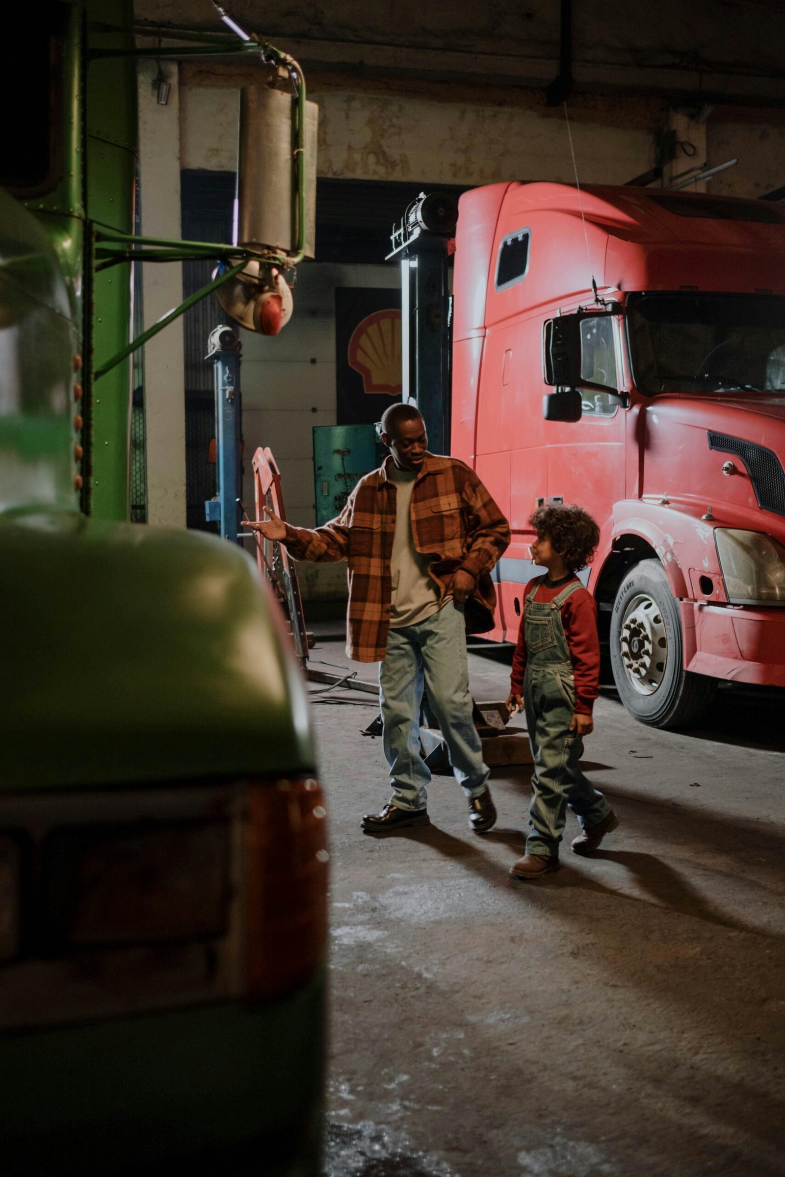Father and child bonding in a garage surrounded by trucks, showcasing family and mechanics.